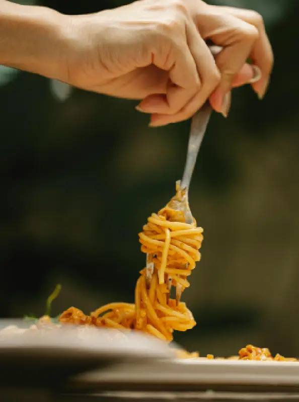 A person holding a fork and knife over some pasta.